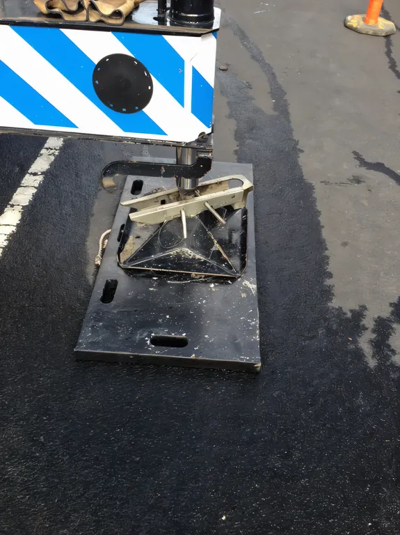 A crane outrigger foot on a black pad on wet asphalt beside a hazard panel