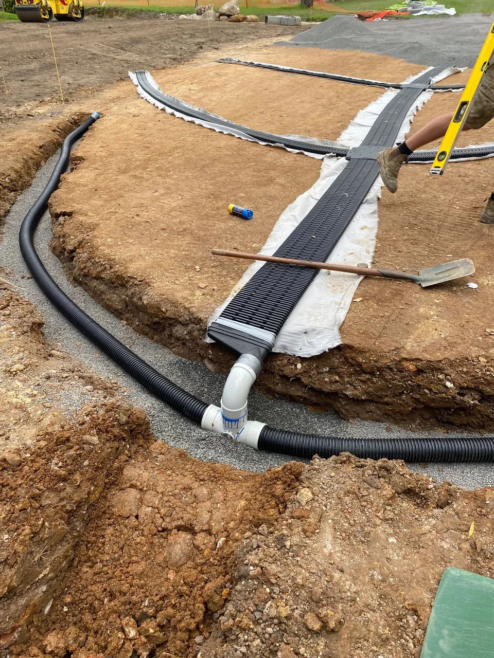 Drainage pipework being laid in a gravel trench on a construction site
