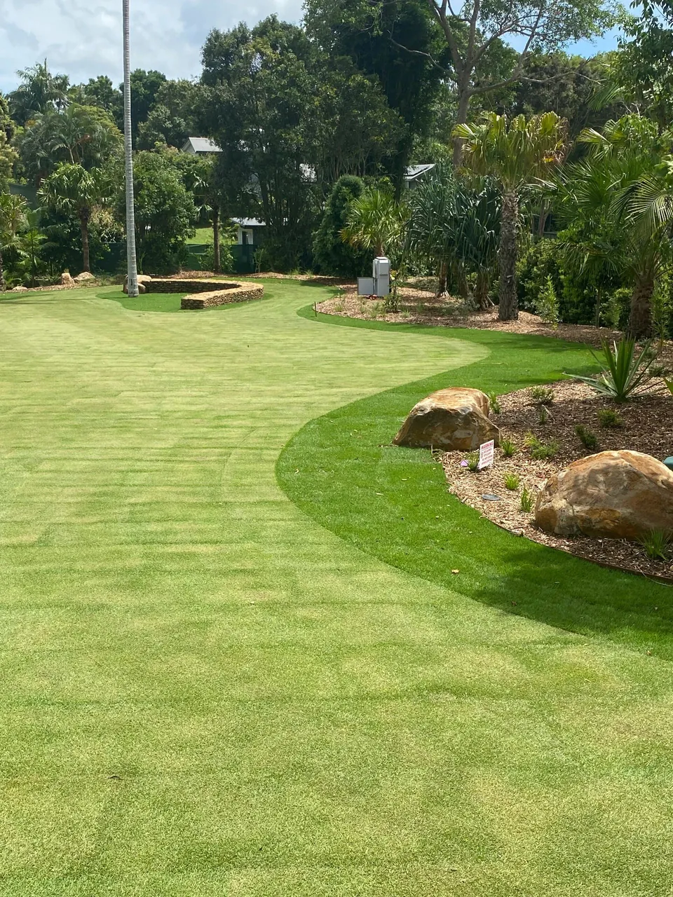A finished lawn with stone edging and palms, freshly irrigated