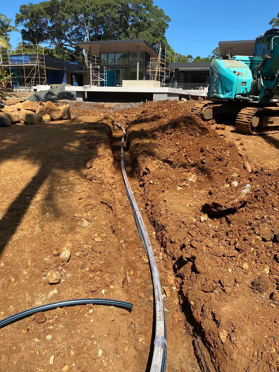 An open trench with black irrigation pipe beside an excavator