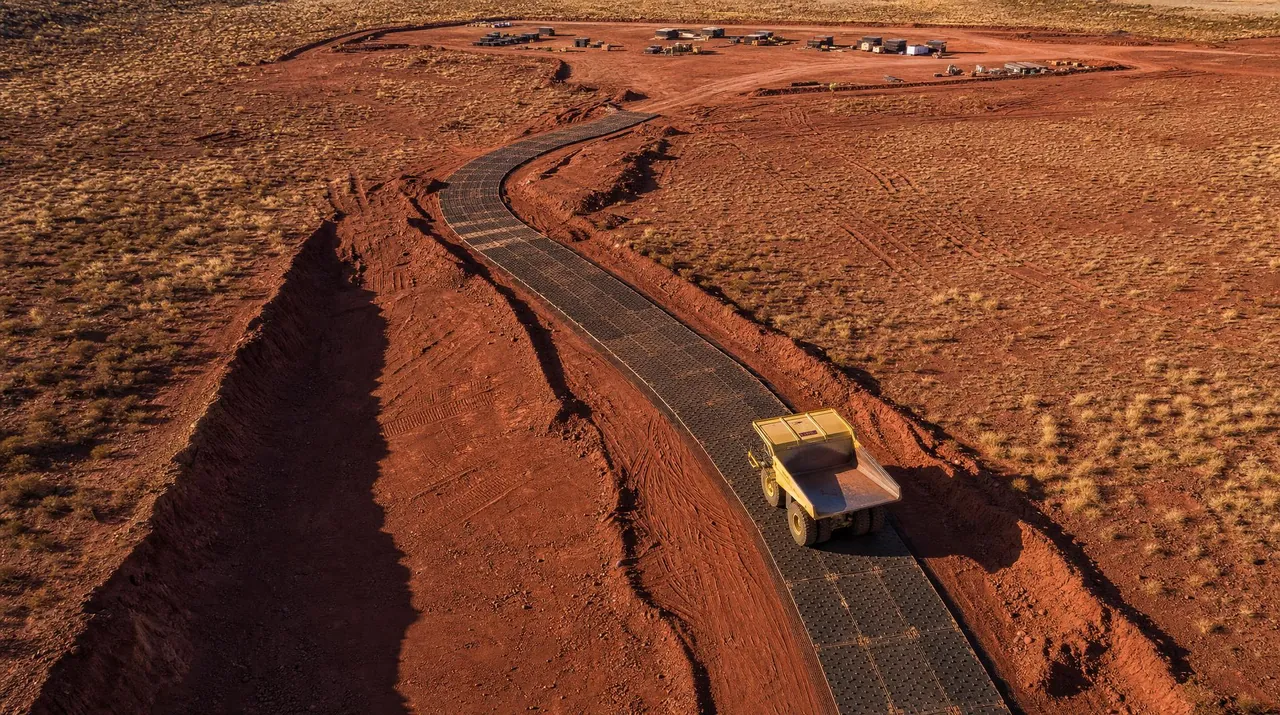 Aerial view of a temporary road of black ground protection mats crossing a red earth mine site